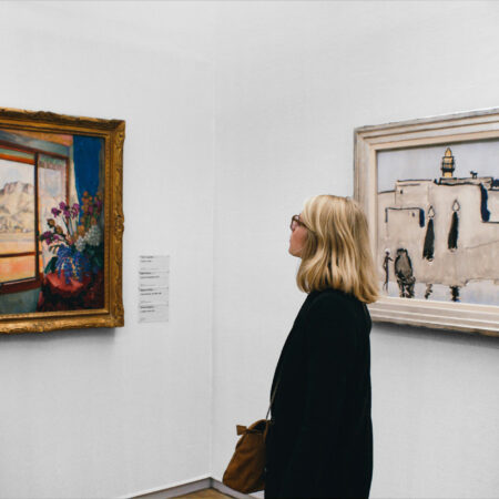 Frau betrachtet Kunstwerke in einem Museum mit einem farbenfrohen Gemälde und einer Landschaftsszene.