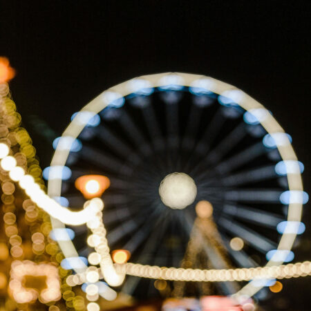 Verschwommene Lichter eines Weihnachtsmarkts mit einem beleuchteten Riesenrad im Hintergrund.