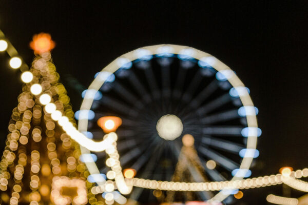 Verschwommene Lichter eines Weihnachtsmarkts mit einem beleuchteten Riesenrad im Hintergrund.