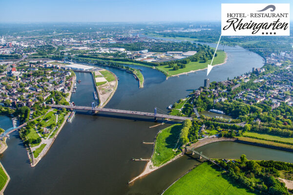 Luftaufnahme von Duisburg mit dem Hotel Rheingarten am Rheinufer, Brücken und umliegenden Grünflächen und Gebäuden.