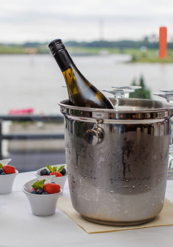 Tisch mit einem Weinkühler, Gläsern und Beeren-Desserts im Hotel Rheingarten in Duisburg mit Blick auf den Rhein.