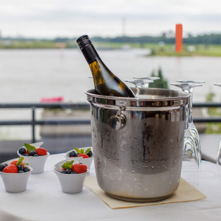 Tisch mit einem Weinkühler, Gläsern und Beeren-Desserts im Hotel Rheingarten in Duisburg mit Blick auf den Rhein.